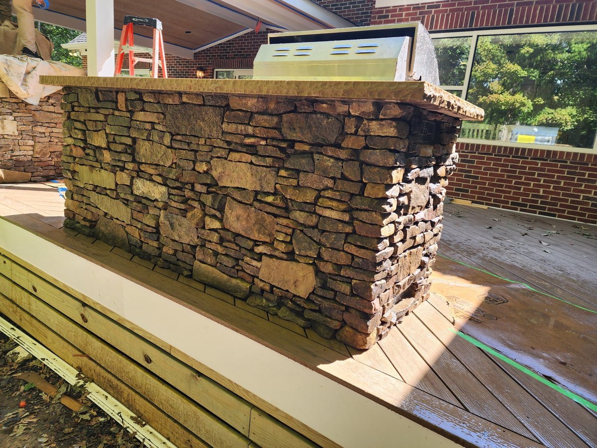 Stone counter and planter feature on a wooden deck with residential house and garden in background