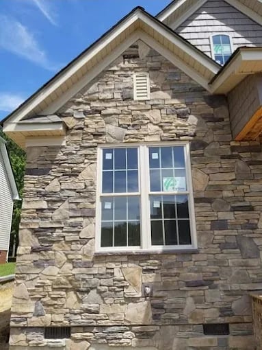 Stone house exterior with large double-pane window, peaked roof, and clear blue sky